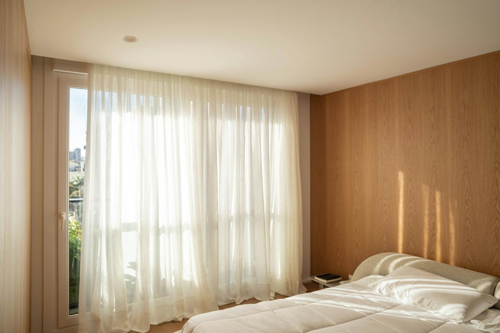 A sunlit bedroom with sheer curtains and warm wood panelling